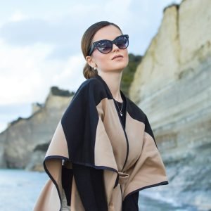 woman wearing black and brown dress and sunglasses standing near body of water under white and blue sky